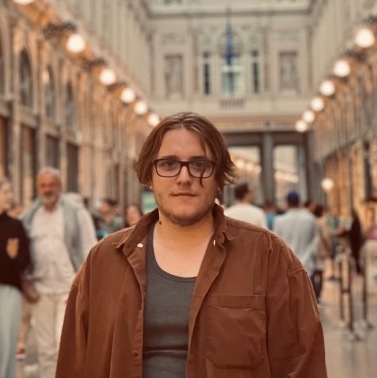 Young man wearing glasses facing the camera and standing in a crowded place